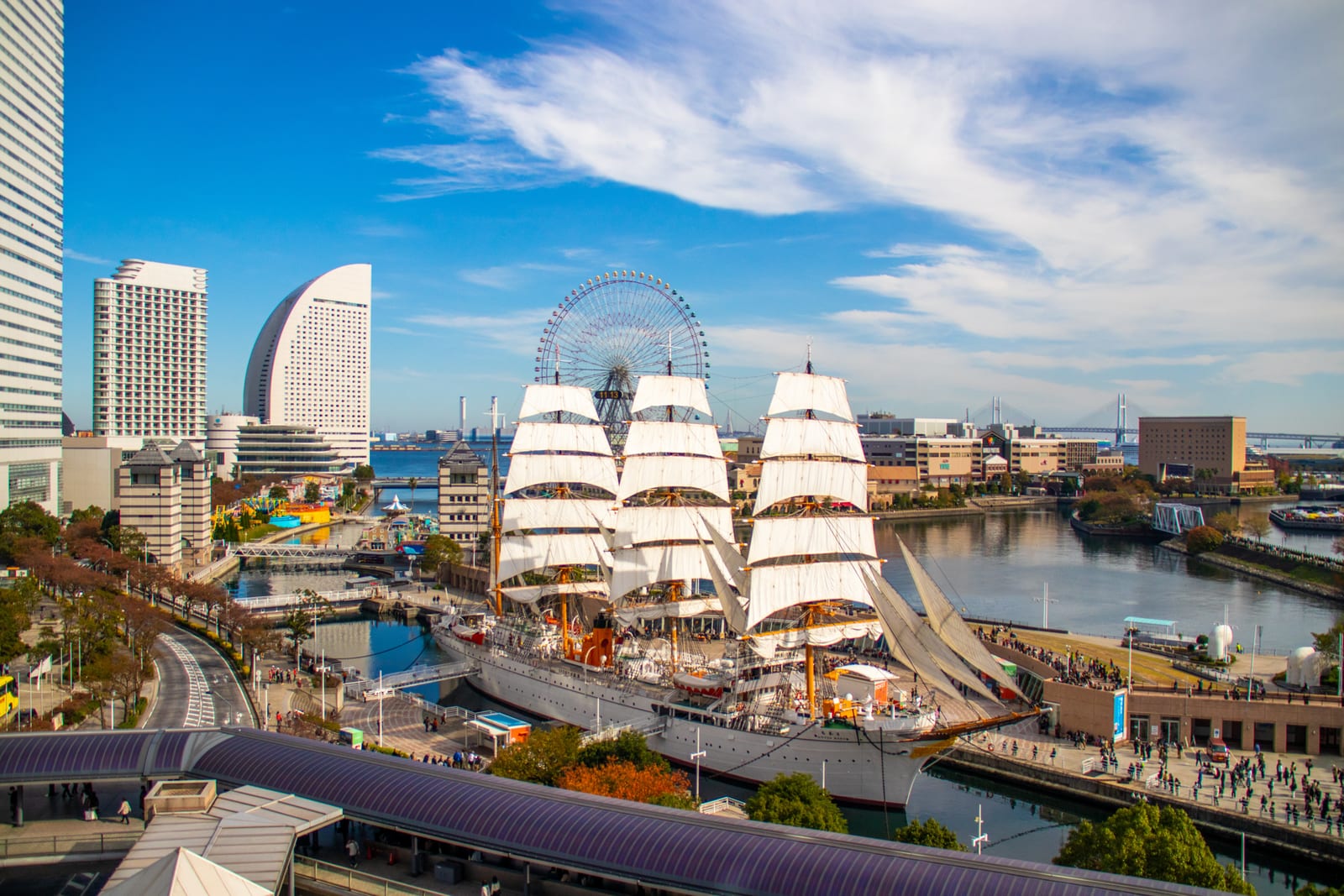 The tall ship Nippon Maru with sails fully raised, the Cosmo Clock Ferris wheel, and the Minato Mirai skyline behind